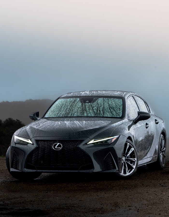 Home Elegant Lexus sedan captured outdoors in Cambria, CA with a misty backdrop and rain-covered vehicle.