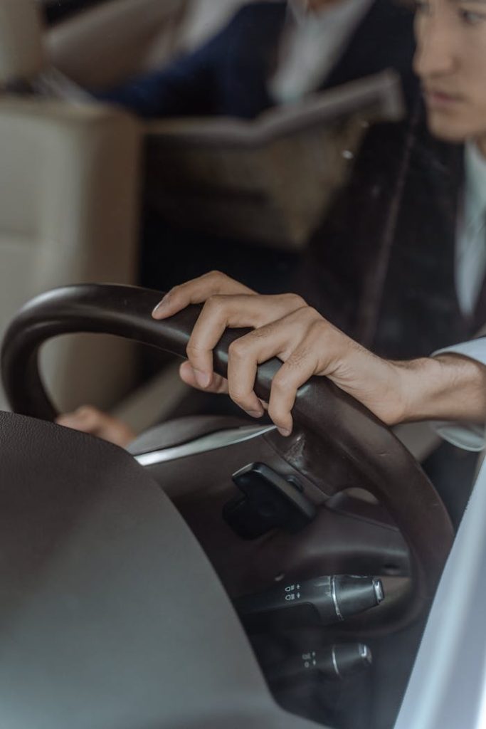 pexels photo 9520197 Close-up shot of a chauffeur's hand on the steering wheel, driving a luxury car interior.